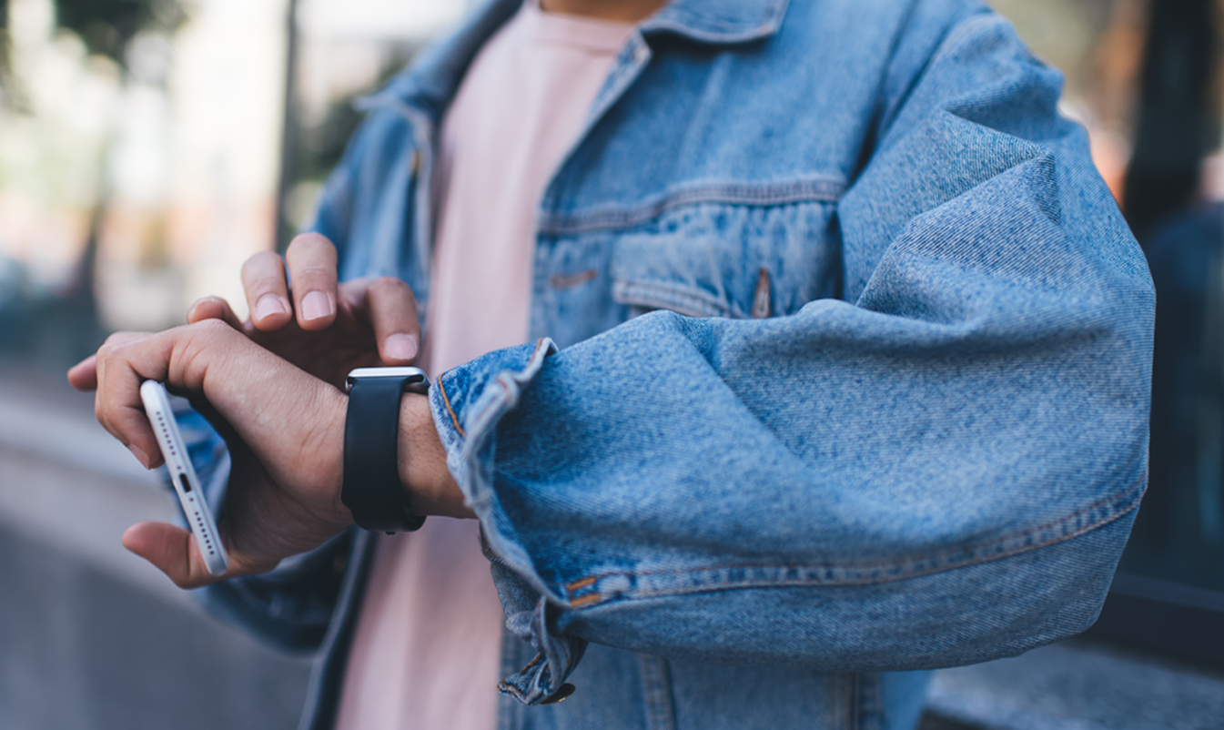 un homme regarde et fait défiler sa smartwatch tout en tenant son téléphone dans l'autre main