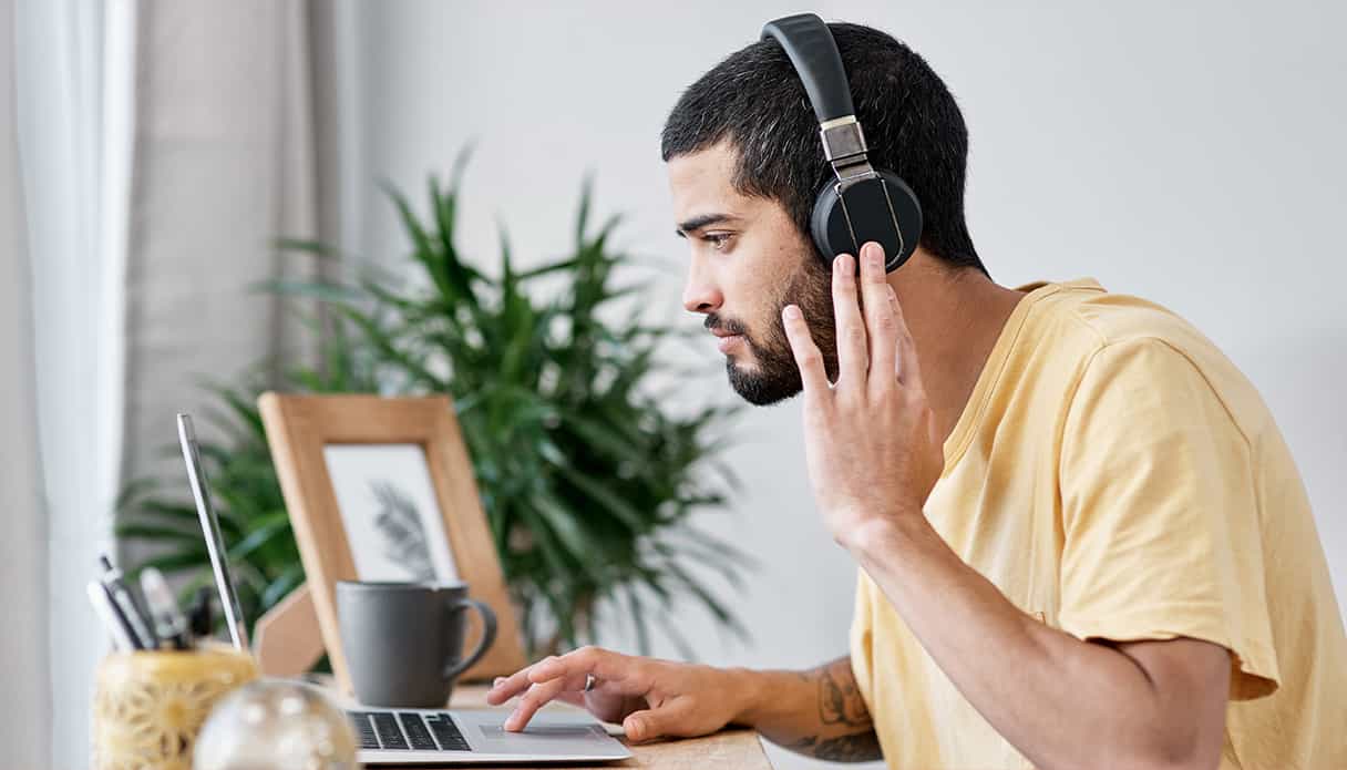 Un homme est assis &agrave; son bureau, regardant son ordinateur portable, tout en portant un casque avec r&eacute;duction de bruit.