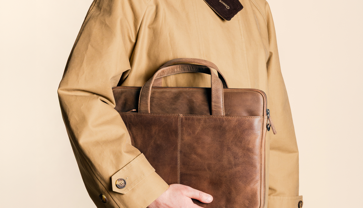 Un homme tient devant lui une housse d'ordinateur portable en cuir couleur cognac.