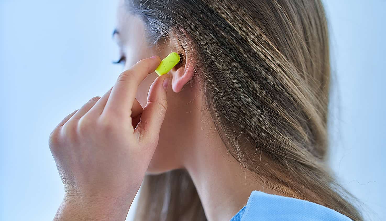 Une femme insère des écouteurs jaune vif dans ses oreilles pour prévenir les dommages auditifs lors d'un festival.