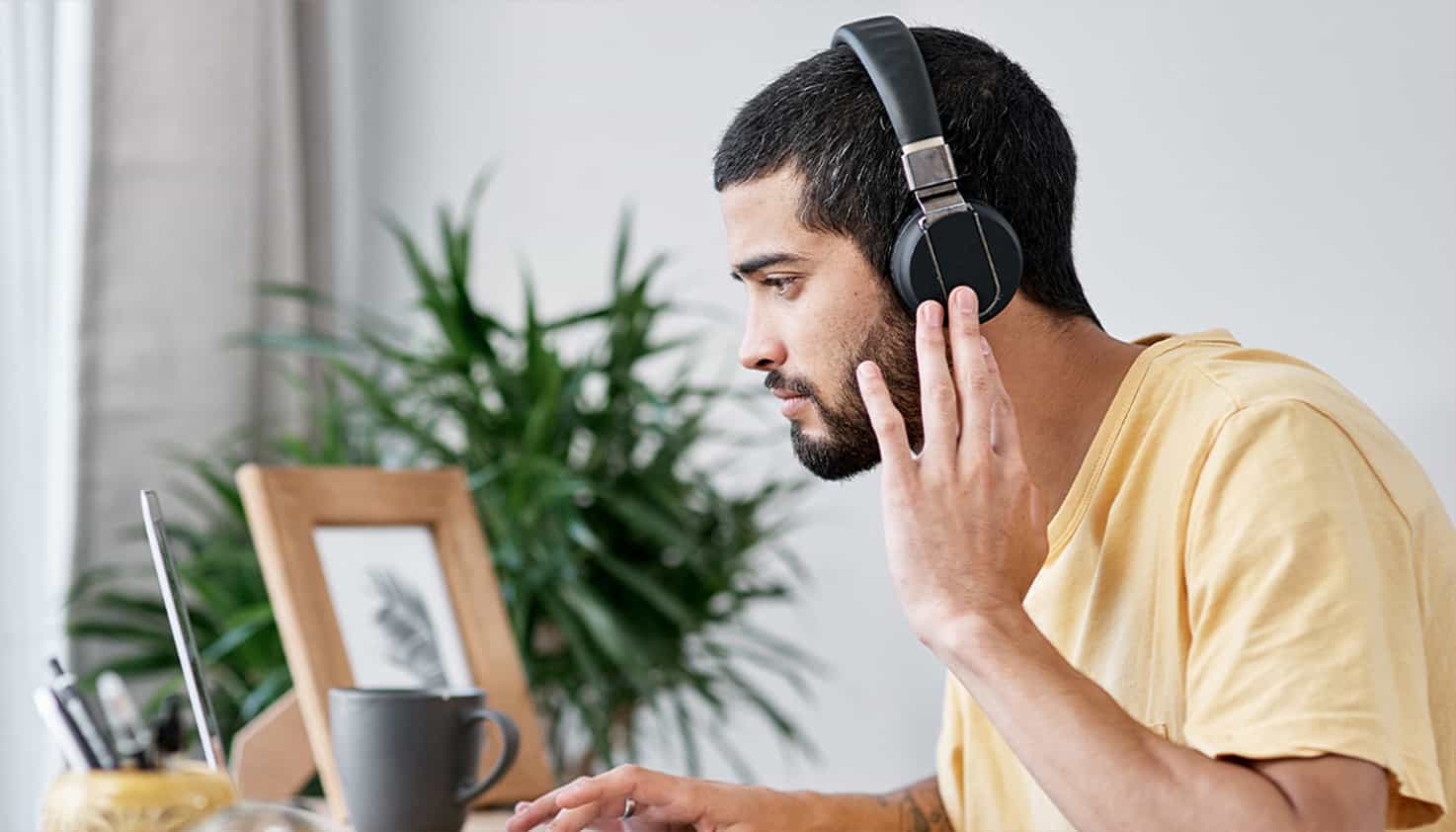 Un homme est assis &agrave; son bureau, regardant son ordinateur portable, tout en portant un casque avec r&eacute;duction de bruit.