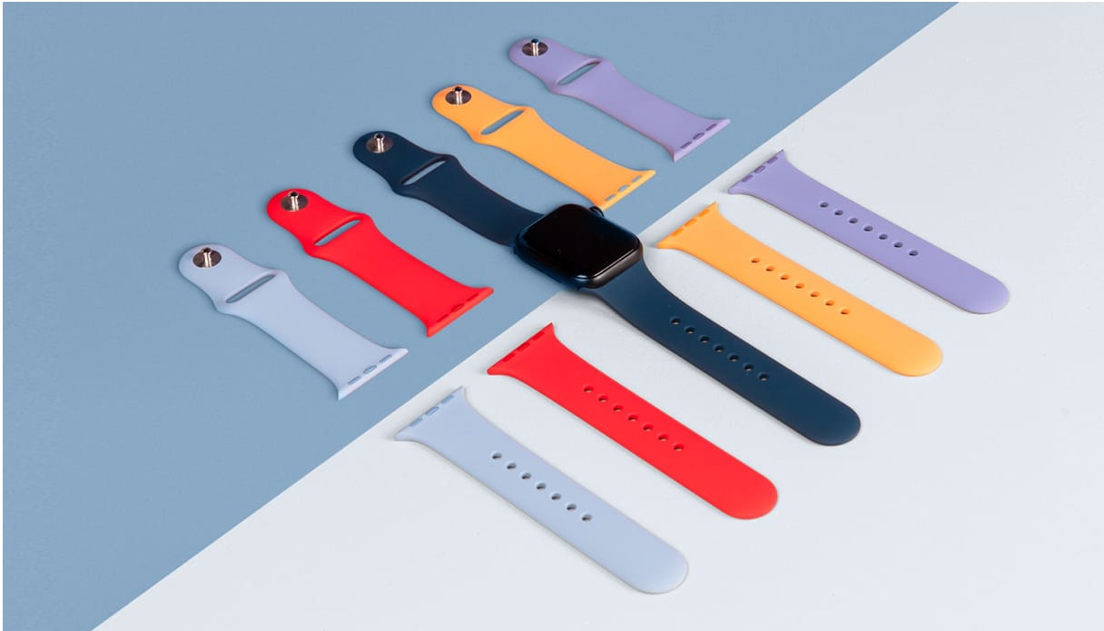On voit une Apple Watch coloris midnight avec un bracelet bleu fonc&eacute;. D'autres bracelets sont dispos&eacute;s &agrave; c&ocirc;t&eacute; de fa&ccedil;on stylis&eacute;e et align&eacute;e, dans diff&eacute;rentes couleurs. Le fond est mi-bleu, mi-blanc.