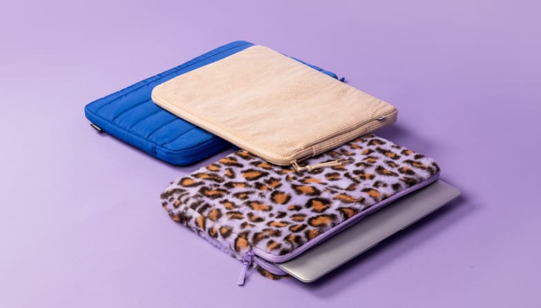 Une housse pour ordinateur portable bleu cobalt, une housse en velours beige et une housse à imprimé léopard violet sont posées côte à côte.