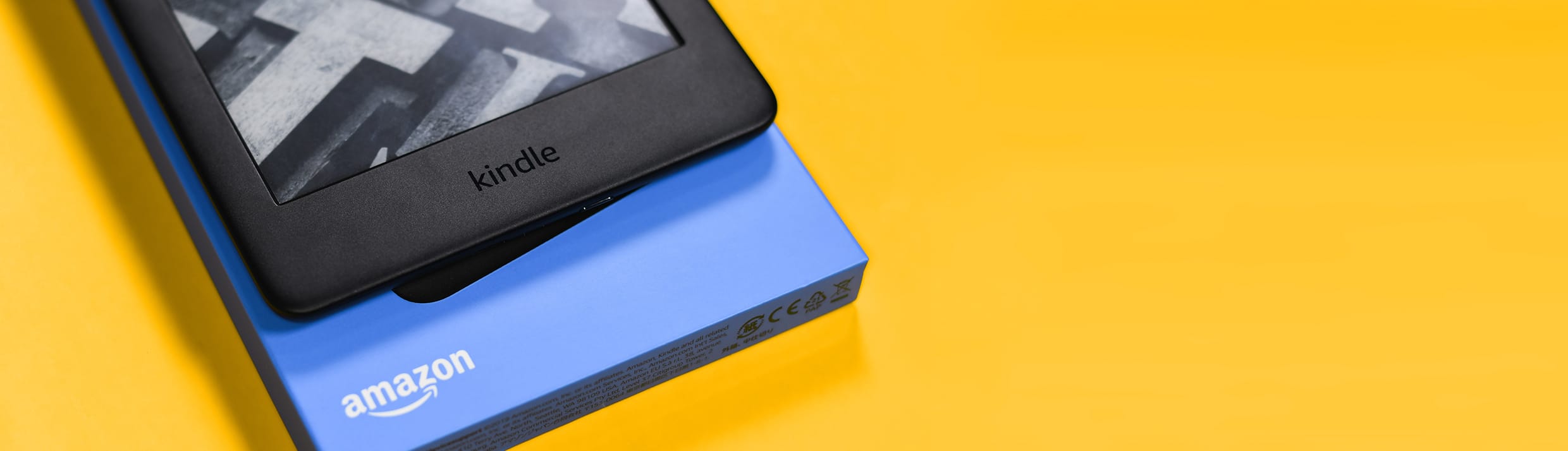 Un Amazon Kindle et son emballage sur fond jaune.