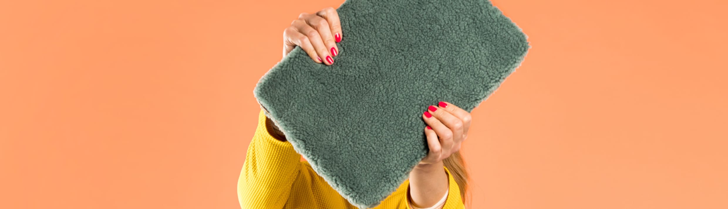 Une femme tient une housse d’ordinateur portable en tissu teddy vert foncé devant son visage.