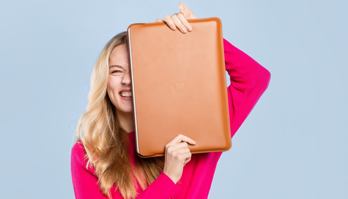 Une femme tient une housse d'ordinateur portable en cuir couleur cognac à moitié devant son visage.