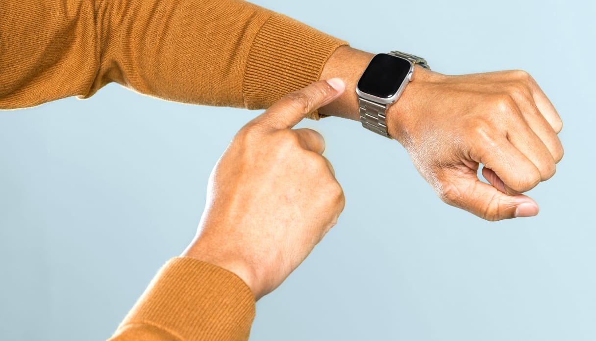 On voit un bras avec une smartwatch au poignet sur un fond bleu clair. Le pull est jaune et la smartwatch est utilis&eacute;e avec l'autre main.