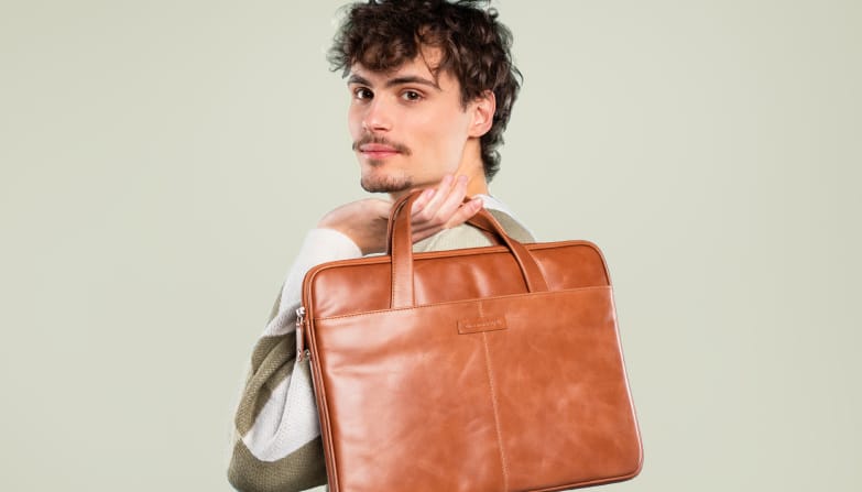 Un homme tient un sac pour ordinateur portable en cuir cognac dans ses mains.