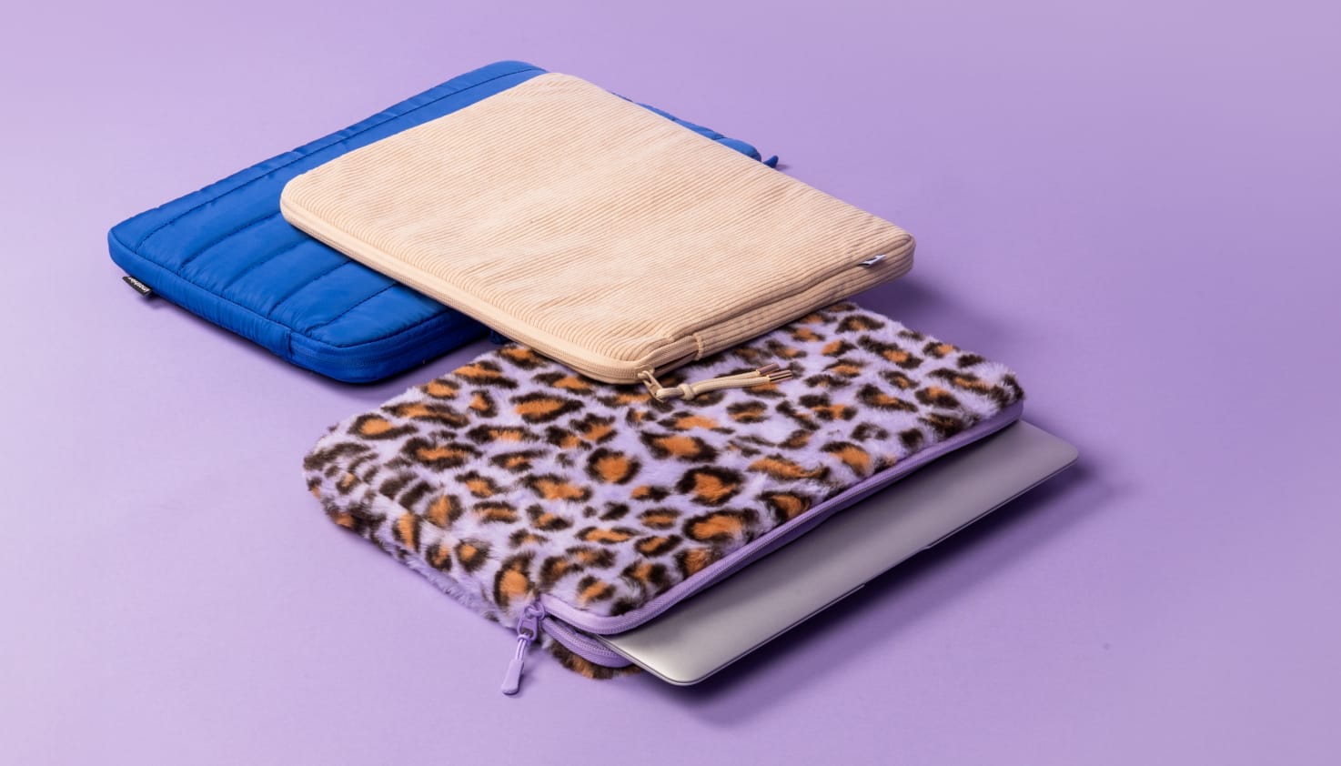 Une housse pour ordinateur portable bleu cobalt, une housse en velours beige et une housse à imprimé léopard violet sont posées côte à côte.