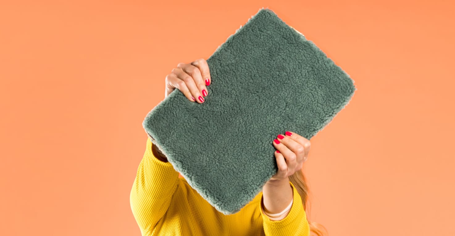 Une femme tient une housse d’ordinateur portable en tissu teddy vert foncé devant son visage.