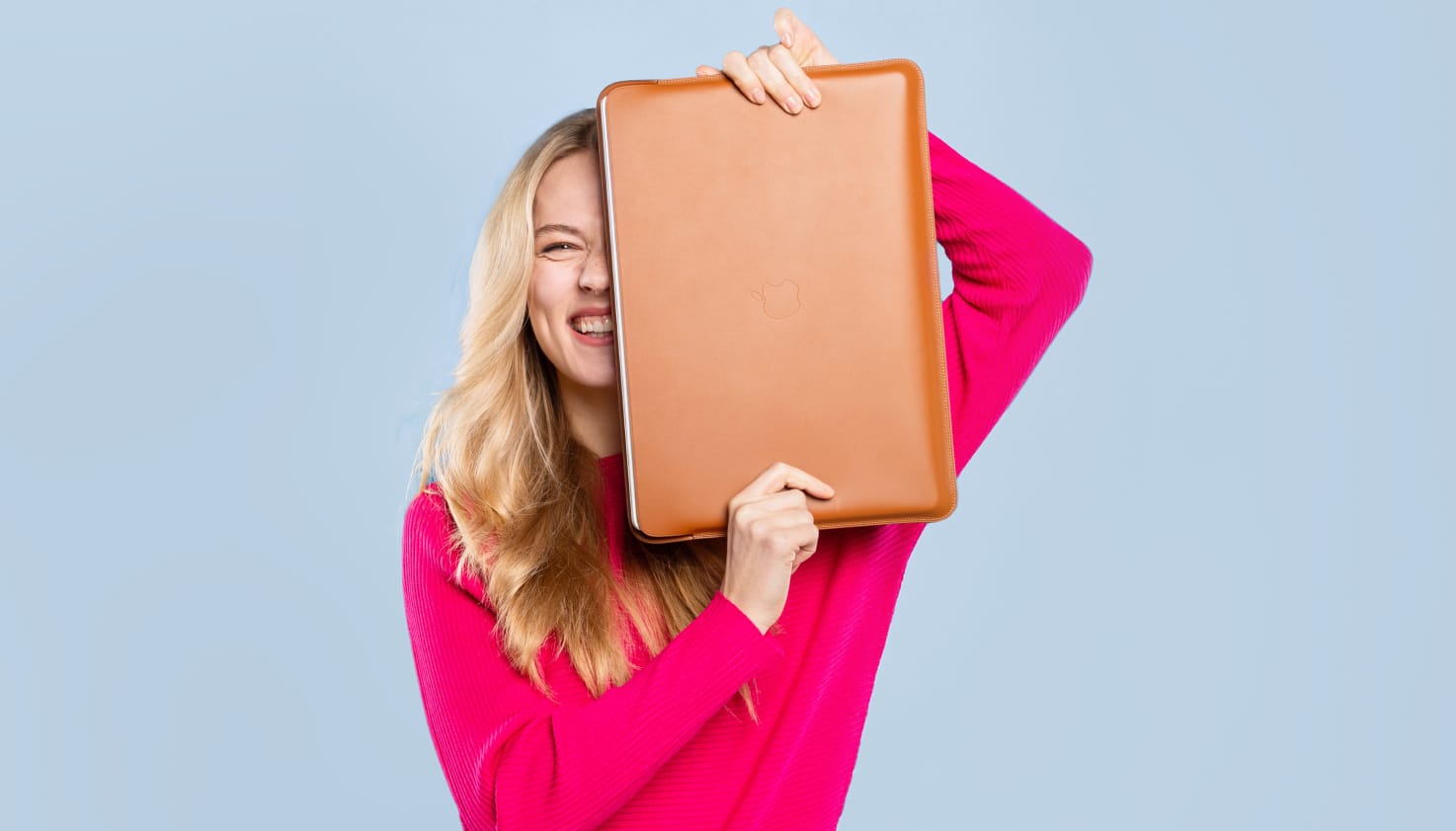 Une femme tient une housse d'ordinateur portable en cuir couleur cognac à moitié devant son visage.