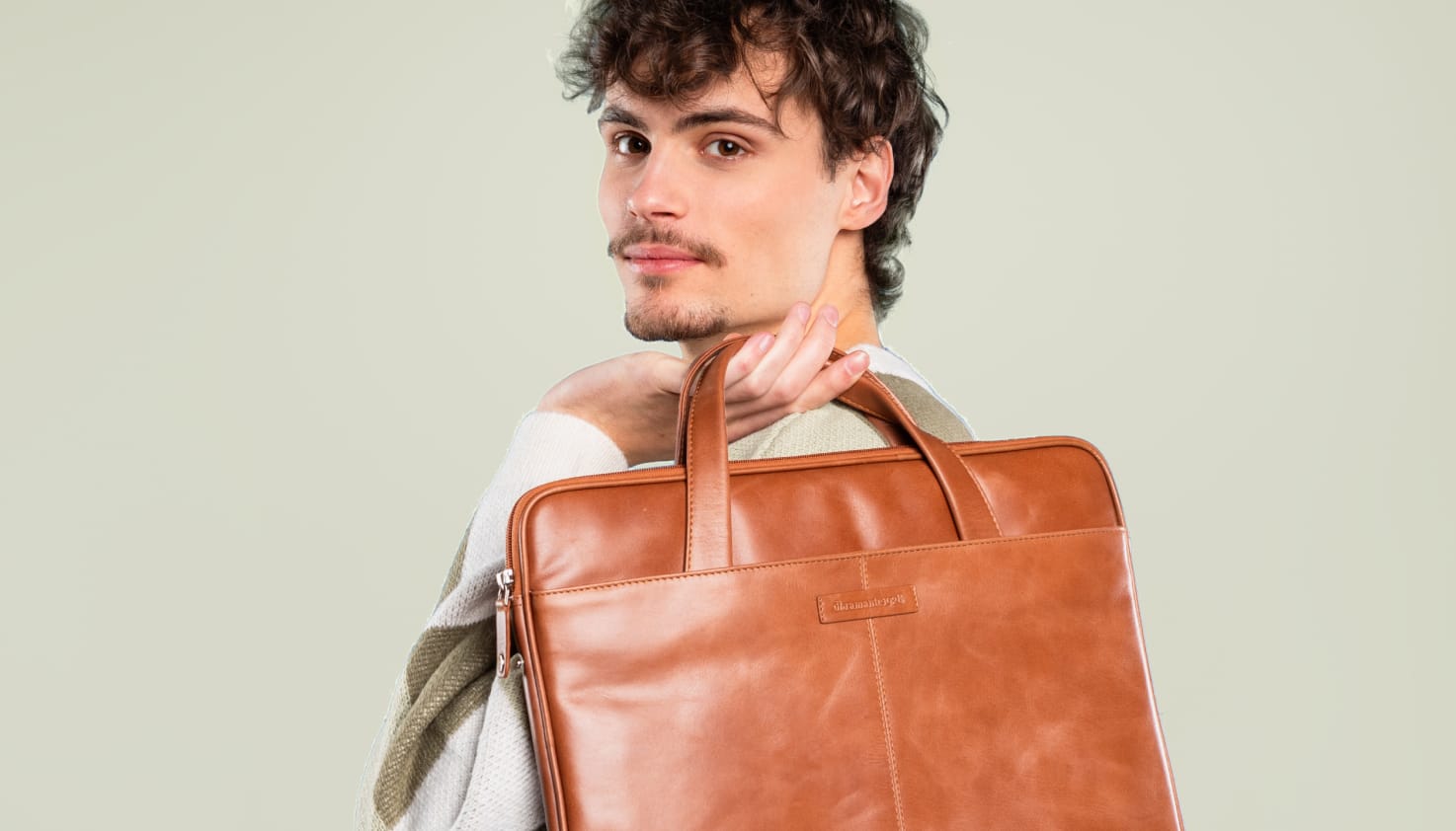 Un homme tient un sac pour ordinateur portable en cuir cognac dans ses mains.